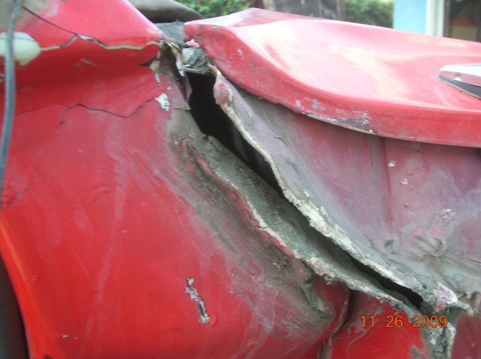Damaged red vehicle fender with visible metal and filler