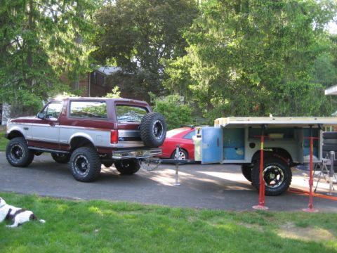 1996 Ford Bronco - A 1996 Ford Bronco is parked next to a trailer, with a red car visible in the background.