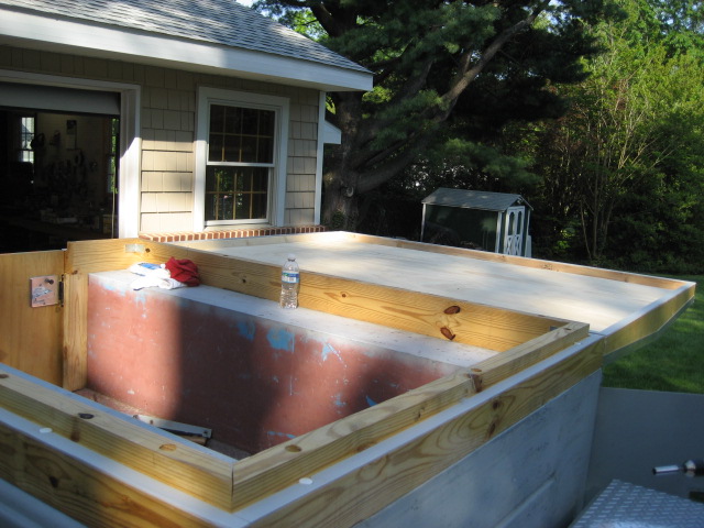 unfinished basement window well with wooden frame and concrete base, next to a house and shed