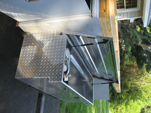 Diamond plate aluminum truck bed tool box with lid open, showing internal storage and gas struts