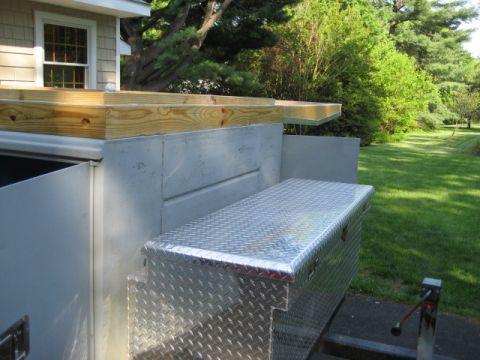 1996 Ford Bronco - A diamond plate aluminum toolbox is mounted on the side of a trailer, with unfinished wood planks stacked above it.