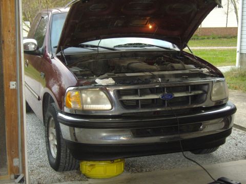 2007 Ford Mustang - A maroon Ford F-150 truck is parked in a garage with its hood open and an oil drain pan underneath.