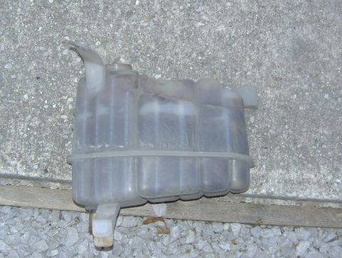 2007 Ford Mustang - A used plastic coolant reservoir tank sits on a gravel surface.