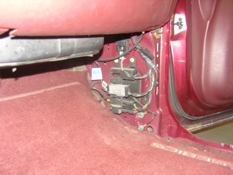2007 Ford Mustang - Close-up of the vehicle's interior fuse box and associated wiring, located on the floor near side of the passenger footwell.