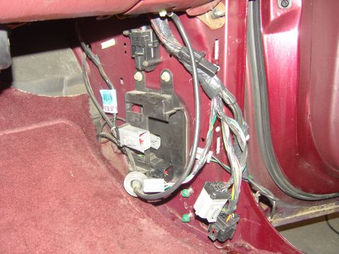 2007 Ford Mustang - Interior teardown at the driver's kick panel of a burgundy vehicle, with the dash trim removed to expose the wiring harness, white and blac…