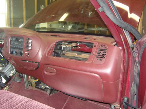 2007 Ford Mustang - Passenger-side view of a burgundy pickup dashboard mid-repair, with the center defroster/speaker grille removed to expose the HVAC ductwork…