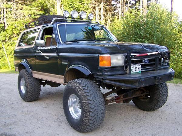 Modified black Ford Bronco with large tires and roof rack, parked outdoors