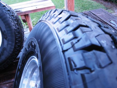 1986 Ford Bronco - Two off-road tires are shown mounted on rims, resting on a wooden deck with grass in the background.