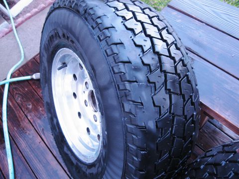 1986 Ford Bronco - A close-up of a tire and wheel assembly, with a garden hose visible on the left.