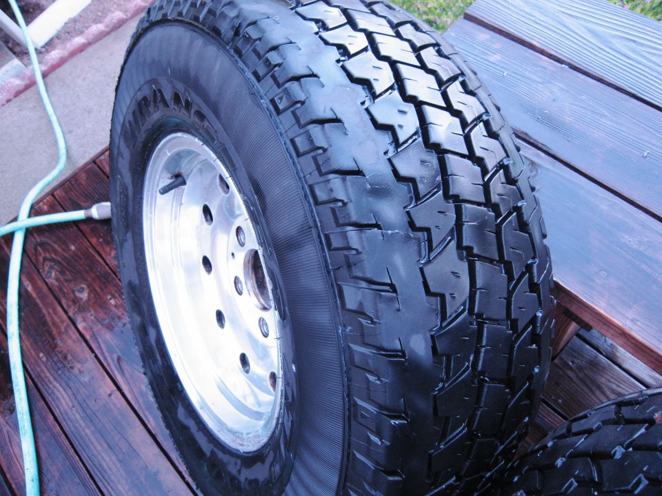 Tire on a silver alloy wheel, resting on a wooden deck with a garden hose nearby