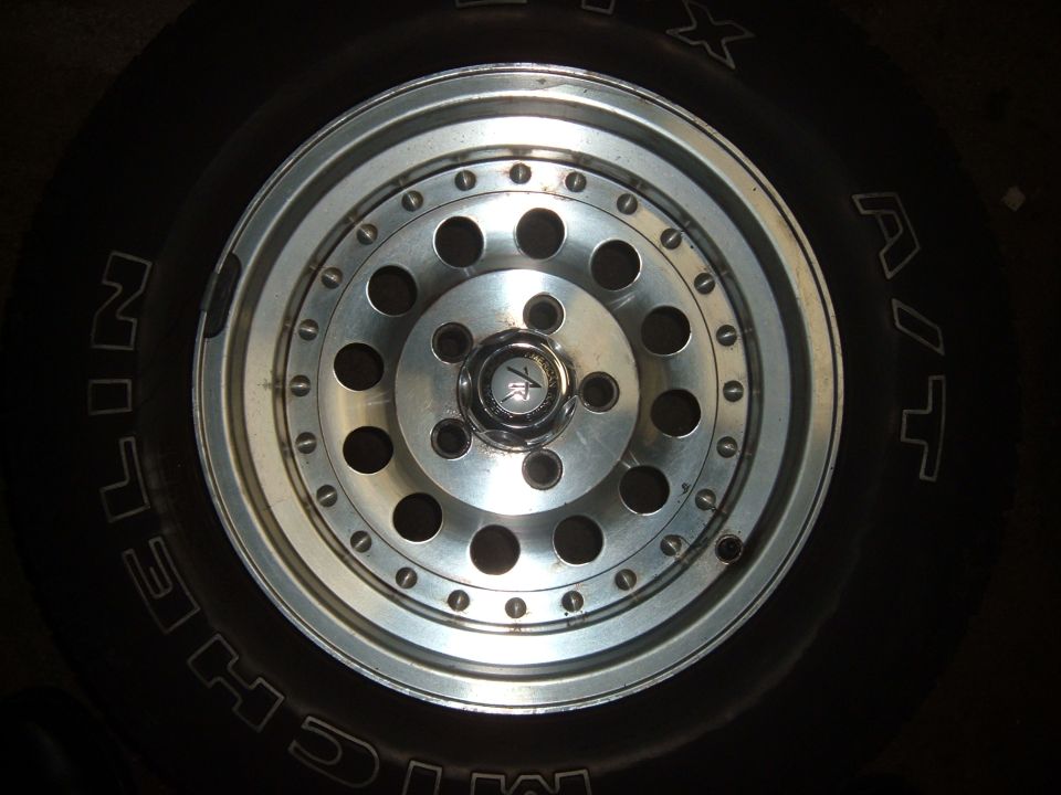 close-up of a silver alloy wheel with many holes, mounted on a black tire with white lettering