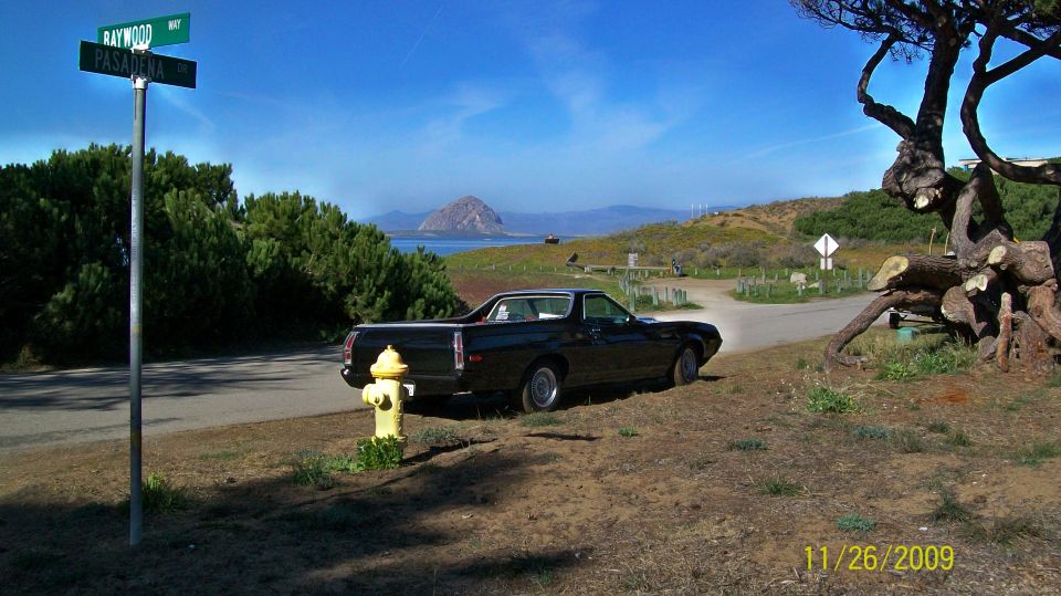 black pickup truck parked by a fire hydrant near a coastal road with a mountain in the background