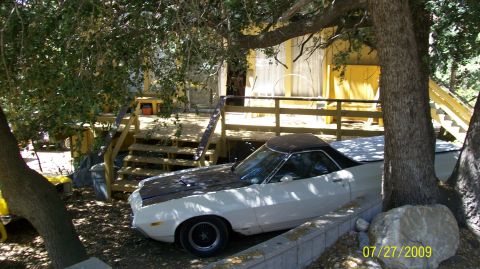 1972 Ford Ranchero - A white 1972 Ford Ranchero with black hood stripes is parked in a shaded, outdoor setting next to a wooden deck.