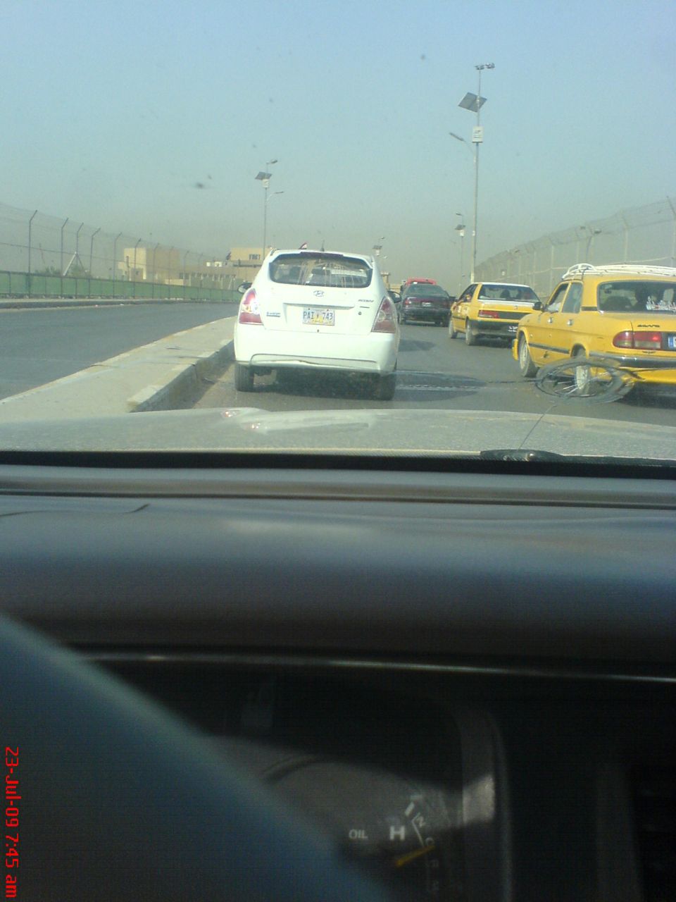 Dashboard view through windshield of traffic with a white hatchback and yellow taxis