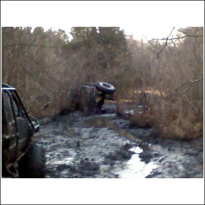 2004 Jeep Wrangler - An off-road vehicle is stuck in the mud and appears to be overturned, with another vehicle partially visible on the left side of the frame.