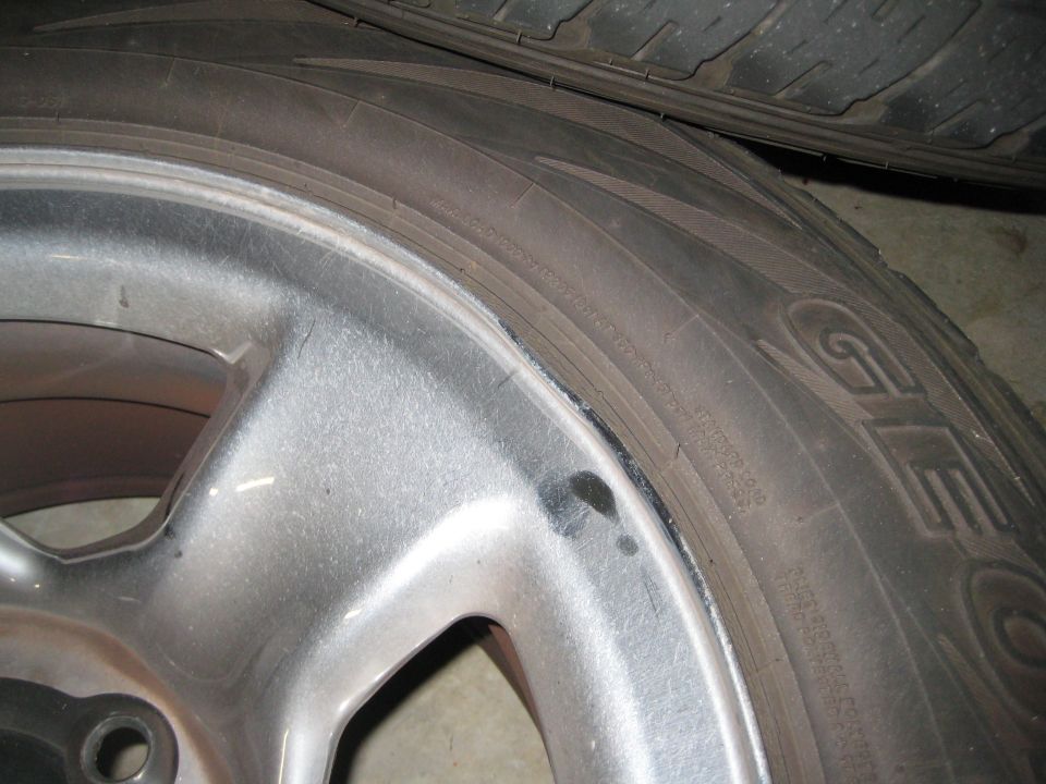 Close-up of a scuffed silver alloy wheel lip and tire sidewall on a concrete floor