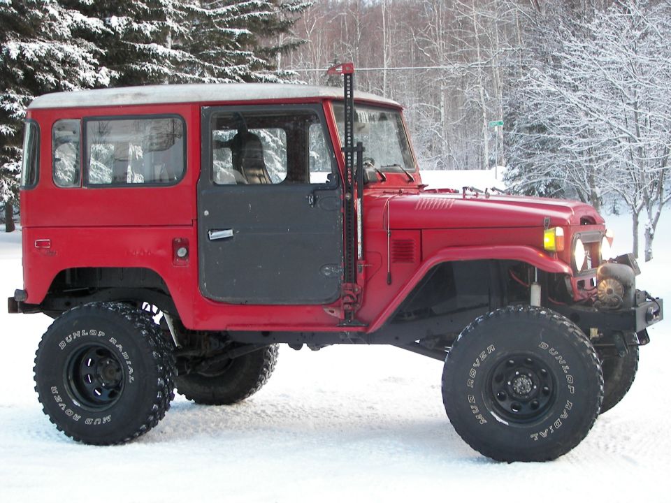 Red Toyota Land Cruiser FJ40 with large off-road tires parked in snow