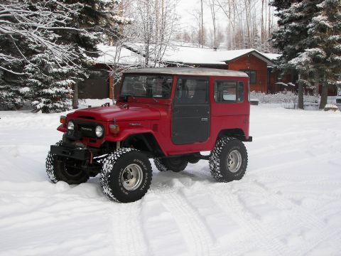 1990 Chevrolet Suburban - This red Toyota Land Cruiser FJ40 is parked in a snowy environment, large off-road tires.