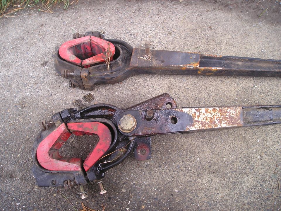 Two suspension radius arms with red bushings, one above the other, resting on concrete