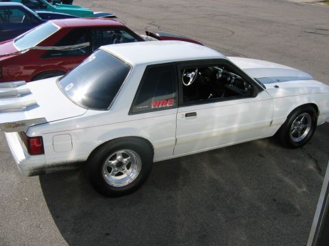 1992 Ford Mustang - White 1992 Ford Mustang coupe with racing stripes and a large rear spoiler parked next to other vehicles.