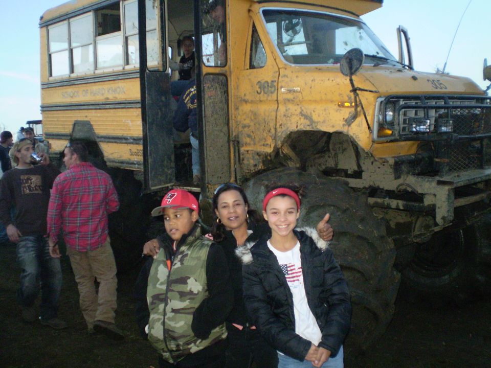 Lifted yellow "School of Hard Knox" school bus monster truck on mud tires with people posing in front