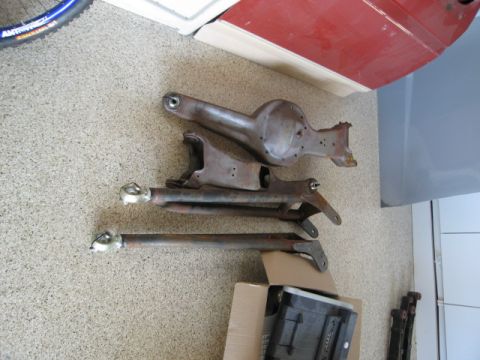 1986 Ford Bronco - Rusty radius arms and differential housing for a 1986 Ford Bronco are laid out on the floor.