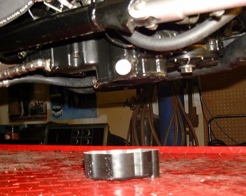 1999 Kawasaki H2C - Close-up view of motorcycle engine components, including hoses and a drain plug, with a metal part resting on a red surface.