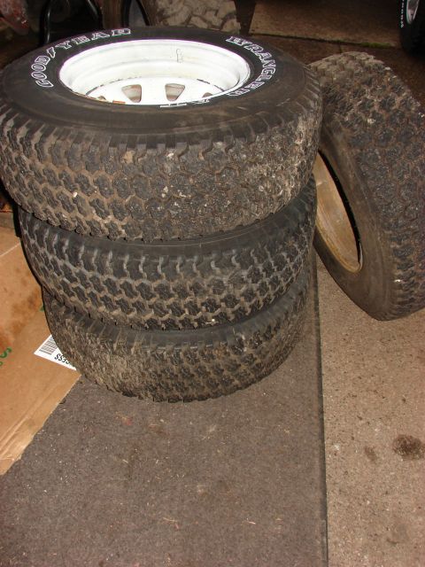 1984 Ford F-250 - Four Goodyear Wrangler tires are stacked, with one mounted on a white wheel, showing signs of use.