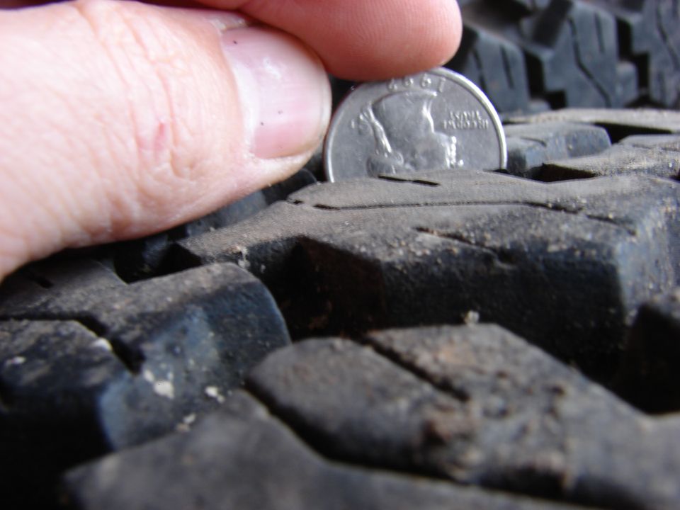 Quarter coin placed in tire tread to show depth