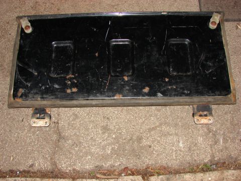 1984 Ford F-250 - This black tailgate features three recessed rectangular areas and shows signs of wear and rust.