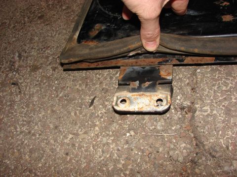 1984 Ford F-250 - A hand presses on a deteriorated rubber door seal attached to a rusty metal bracket on the ground.