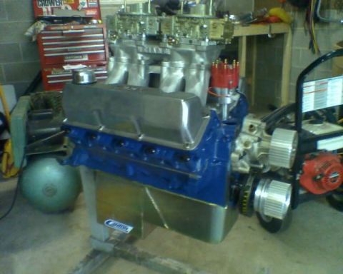 1982 Ford F-100 - Engine assembly with chrome valve covers and dual carburetors sits on a stand in a garage.