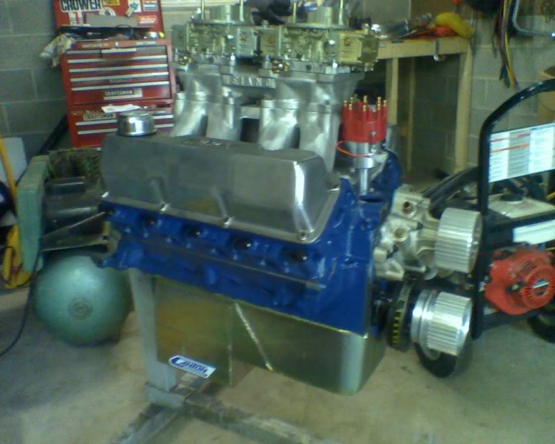 Blue V8 engine with chrome valve covers and dual carburetors on a stand