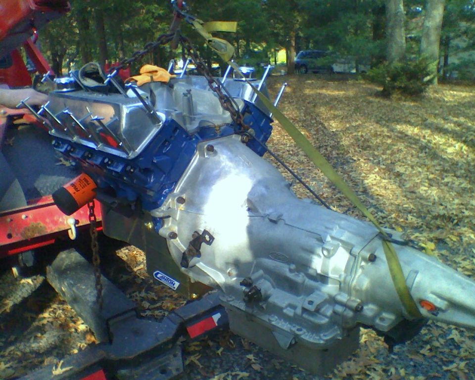 Blue V8 engine and automatic transmission lifted by a chain outdoors