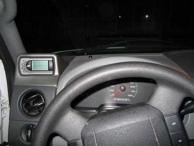 Dashboard of a truck with a steering wheel, speedometer, and a small digital display unit mounted on the dash