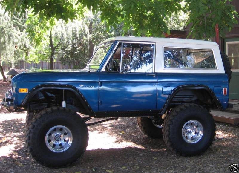 Lifted blue Ford Bronco with white hardtop on large off-road tires, side view