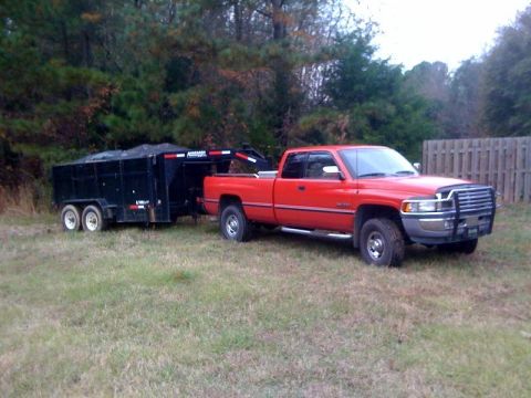 1989 Ford Bronco - A red pickup truck is seen towing a black trailer in a grassy area with trees in the background.