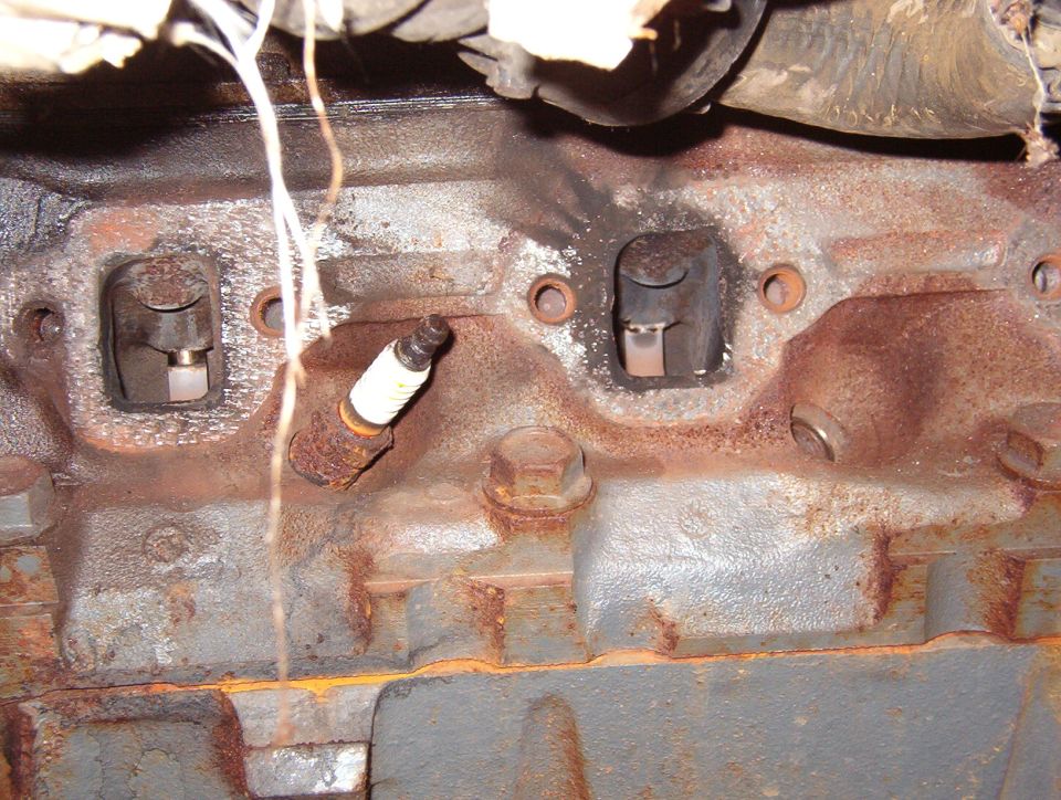 Rusty cylinder head exhaust ports with old spark plug, underside view