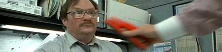 1977 Ford Mustang II - A man wearing glasses and a mustache reacts as a hand offers him a red stapler in an office setting.