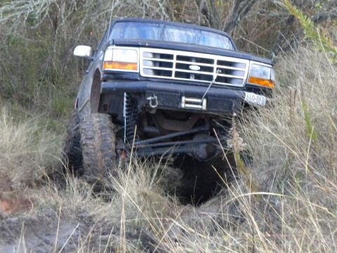 1995 Ford Bronco - A black Ford Bronco with a lifted suspension is stuck in dry grass, viewed from the front.