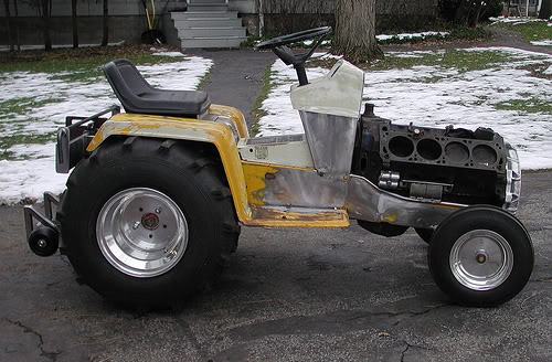 Custom tractor build with a V8 engine block exposed, large rear tires, and small front wheels