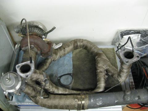 1994 Ford Probe - Turbocharger and exhaust manifold assembly, wrapped in heat shielding, sits on a workbench.