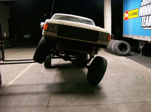 1989 Ford Bronco - White Ford Bronco being lifted by a forklift, showing its front end and suspension.