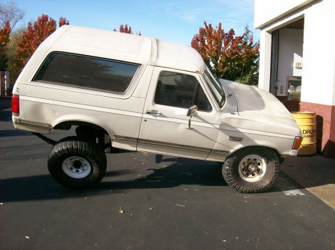 1989 Ford Bronco - White 1989 Ford Bronco with lifted suspension is parked outside a building.