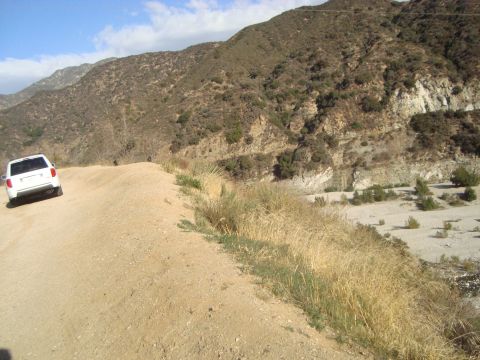 1986 Ford Bronco - A white SUV navigates a dusty, winding road through a , arid mountain landscape.