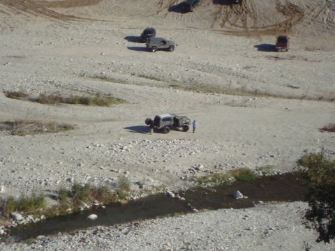 1986 Ford Bronco - Multiple vehicles are parked in a rocky, dry riverbed with a small stream running through it.