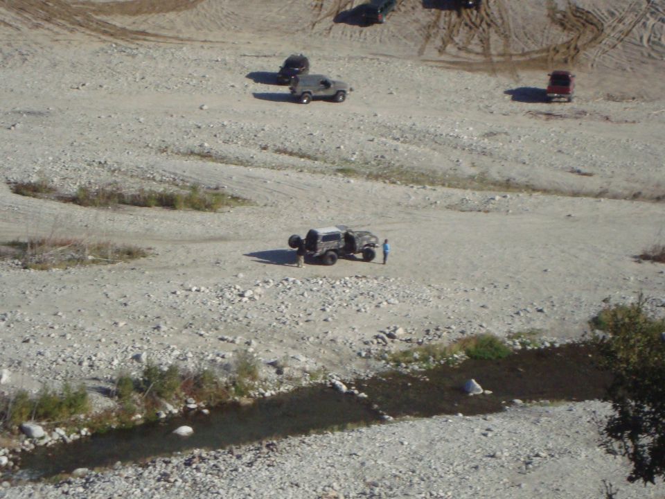 Several off-road vehicles in a dry riverbed with a small stream