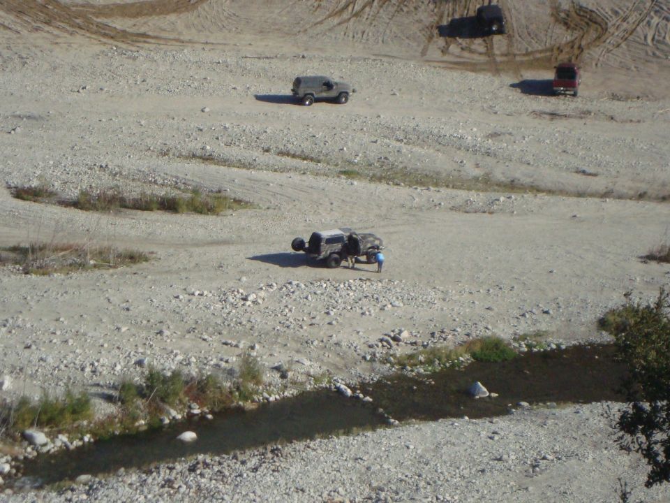 Four-wheel drive vehicles traversing a rocky, dry landscape with a small stream