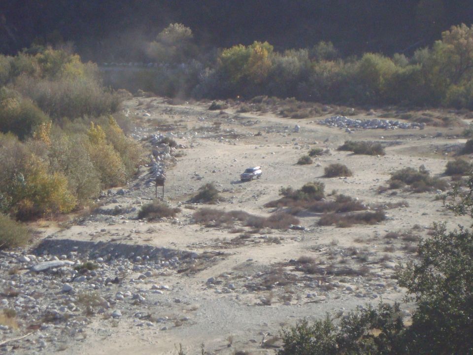 SUV in a dry riverbed with brush and trees