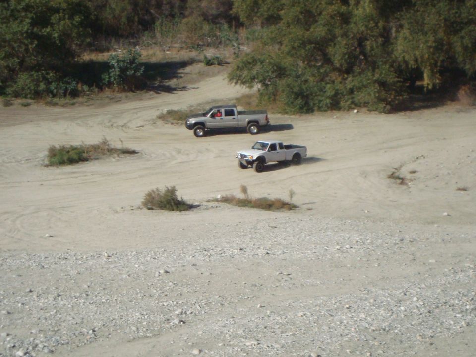 Two pickup trucks on a dirt road, one silver, one white